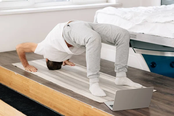 Homme faisant un exercice de pont sur tapis de fitness près d'un ordinateur portable — Photo de stock