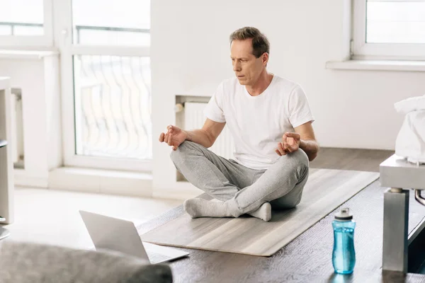 Selektiver Fokus des Mannes in Socken, der in Lotus-Pose sitzt, während er Online-Übungen am Laptop verfolgt — Stockfoto