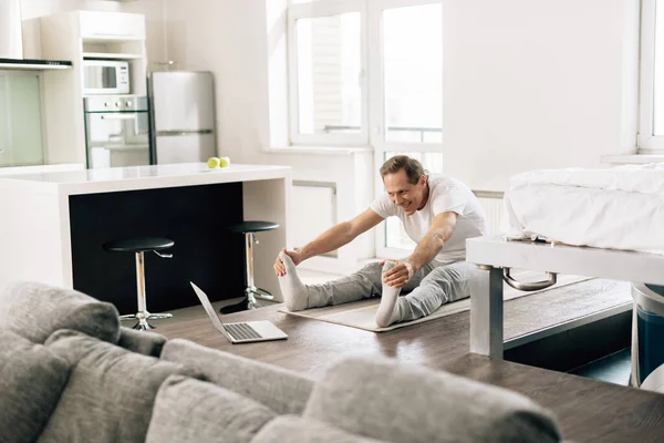 Enfoque selectivo del hombre feliz estiramiento y viendo ejercicio en línea en el ordenador portátil en casa - foto de stock