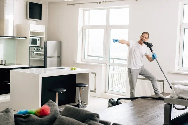 Selektiver Fokus des glücklichen Mannes, der mit dem Finger zeigt, während er singt und Staubsauger hält — Stockfoto