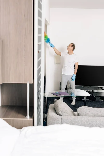 Selective focus of cheerful man holding duster brush while cleaning living room — Stock Photo