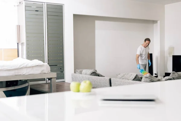 Foco seletivo de homem alegre segurando escova de espanador enquanto a limpeza sofá na sala de estar — Fotografia de Stock