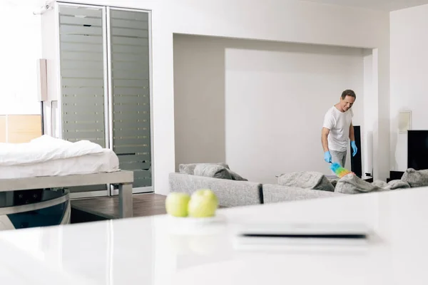 Selective focus of cheerful man holding duster brush while cleaning sofa in living room — Stock Photo