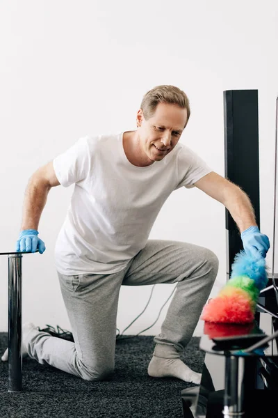 Enfoque selectivo del hombre alegre sosteniendo cepillo de plumero mientras limpia apartamento - foto de stock