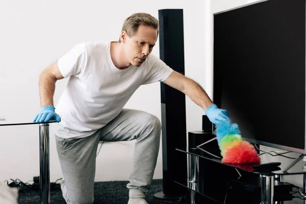 Hombre sosteniendo cepillo de plumero mientras limpia la pantalla de televisión en blanco en la sala de estar - foto de stock