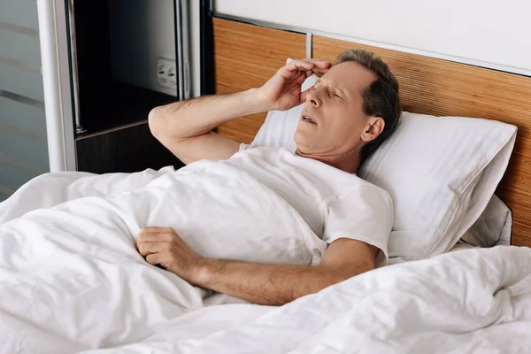 Хворий чоловік лежить на ліжку і торкається голови — стокове фото