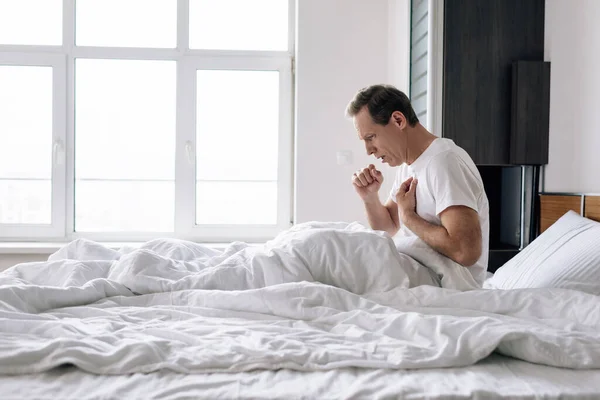 Боковой вид больного человека, кашляющего, сидя дома на кровати — стоковое фото