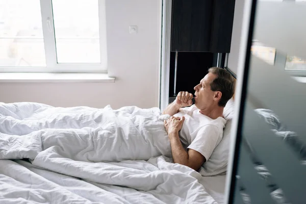 Enfoque selectivo del hombre enfermo toser mientras está acostado en la cama en casa - foto de stock