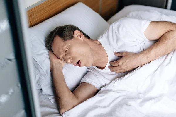 Vista aérea del hombre enfermo tosiendo mientras está acostado en la cama - foto de stock