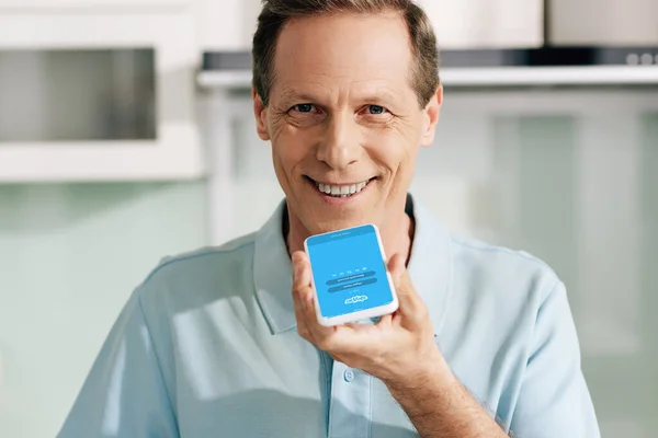 KYIV, UCRANIA - 14 DE ABRIL DE 2020: hombre feliz sosteniendo el teléfono inteligente con la aplicación de Skype en la pantalla - foto de stock