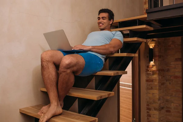 Émotionnel mixte homme utilisant ordinateur portable sur les escaliers à la maison en quarantaine — Stock Photo