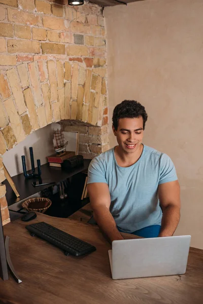 Счастливый фрилансер смешанных рас, работающий с ноутбуком в домашнем офисе во время самоизоляции — стоковое фото