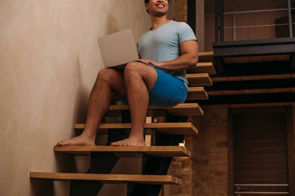 Cropped view of mixed race man using laptop on stairs at home on quarantine — Stock Photo