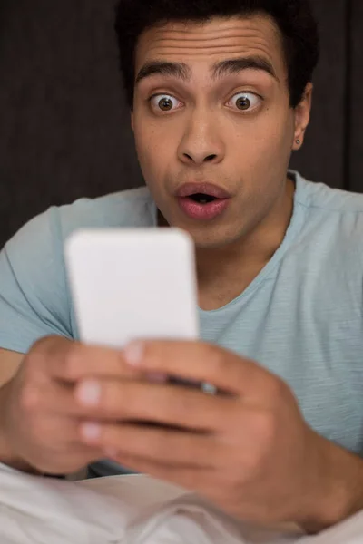 Shocked young mixed race man using smartphone, selective focus — Stock Photo