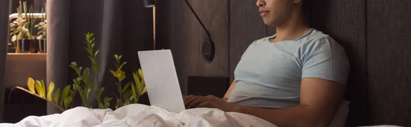 Vista ritagliata di uomo razza mista telelavoro sul computer portatile a letto durante l'isolamento di sé, intestazione del sito web — Stock Photo
