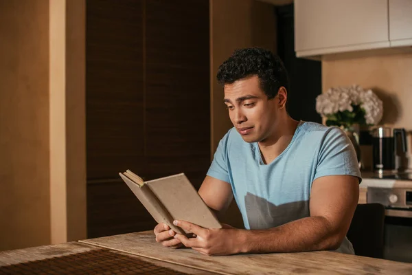 Emotional mixed race man reading book on kitchen during quarantine — Stock Photo