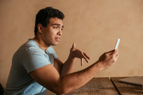 Joven hombre de raza mixta teniendo videollamada en el teléfono inteligente en casa en cuarentena - foto de stock