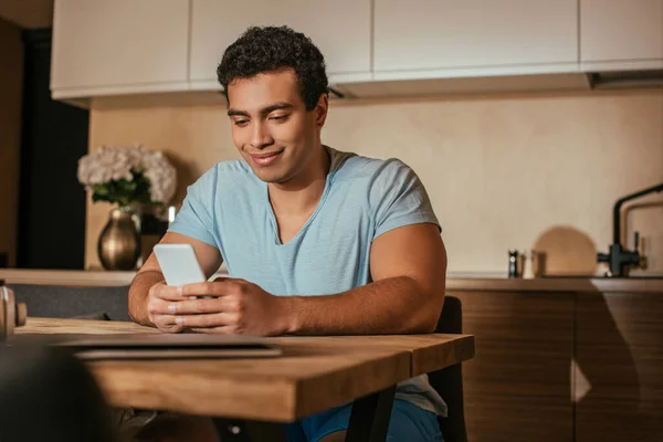 Jeune homme métis utilisant un smartphone sur la cuisine pendant la quarantaine — Photo de stock