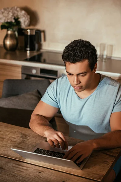 Beau mâle mixte course pigiste travaillant avec ordinateur portable sur la cuisine pendant l'isolement personnel — Photo de stock