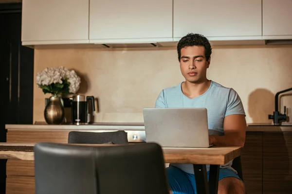 Beau mâle mixte freelance travail avec ordinateur portable sur la cuisine pendant la quarantaine — Photo de stock