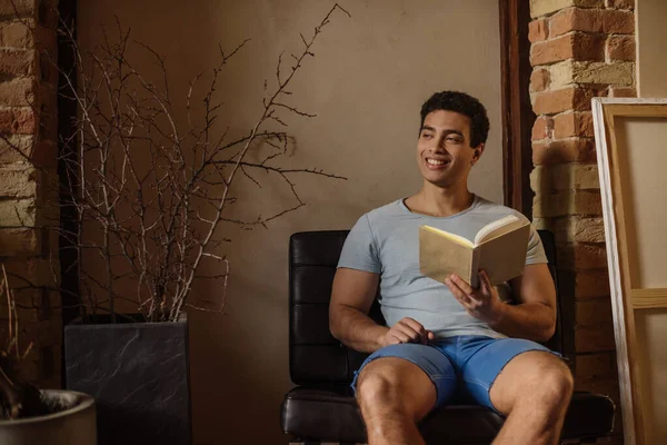Усміхнений красивий чоловік читає книгу вдома під час карантину — стокове фото