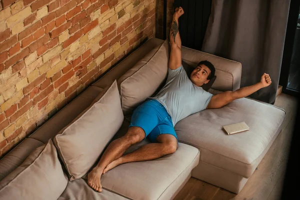 Handsome mixed race man stretching on sofa in living room during quarantine — Stock Photo