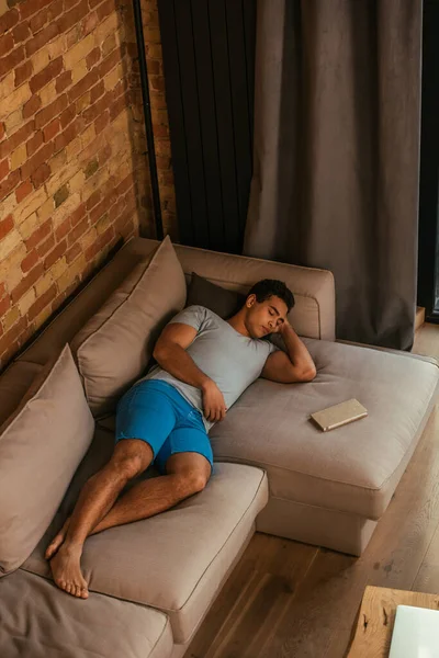 Hombre de raza mixta durmiendo en el sofá con libro en casa durante la cuarentena - foto de stock