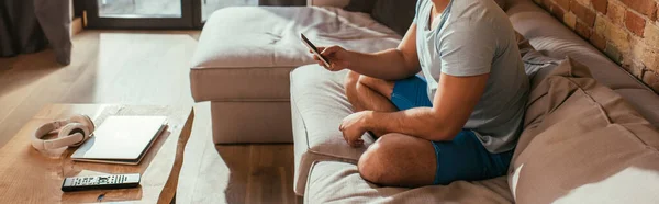 Ausgeschnittene Ansicht eines jungen Mannes, der während der Quarantäne auf dem Sofa chillt und sein Smartphone benutzt, horizontales Konzept — Stockfoto