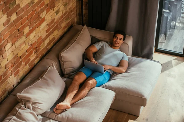 Emotional mixed race man using laptop on sofa at home on quarantine — Stock Photo