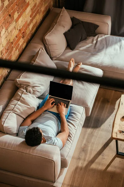 Overhead view of young man using laptop with blank screen while relaxing on sofa at home on quarantine — Stock Photo