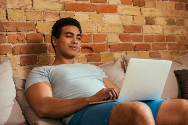 Young bi-racial man chilling with laptop on sofa during self isolation — Stock Photo