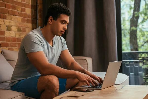 Freelance bi-razziale che lavora con il computer portatile sul divano durante l'isolamento personale — Foto stock