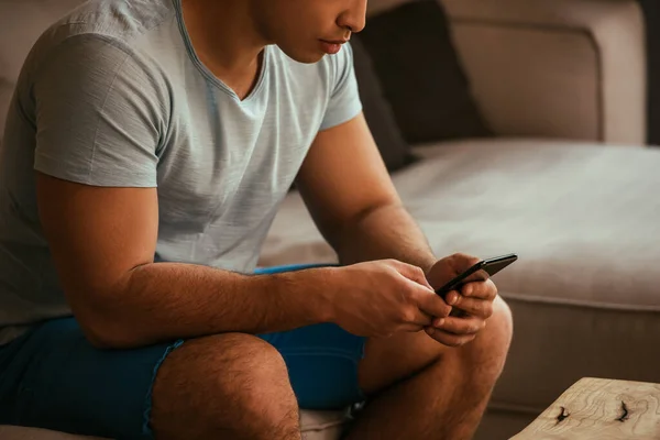 Vista ritagliata di giovane utilizzando smartphone sul divano durante l'isolamento — Foto stock