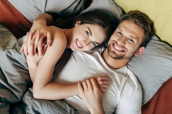 Vista superior de feliz pareja abrazándose en la cama y mirando a la cámara - foto de stock