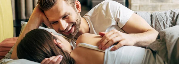 Panoramic shot of cheerful bearded man looking at girlfriend in bed — Stock Photo