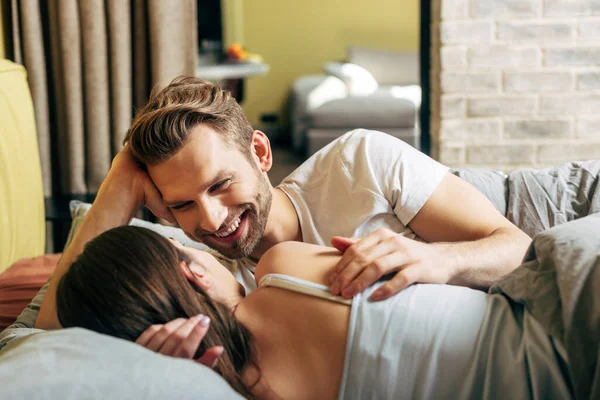 Избирательный фокус счастливого бородатого мужчины, смотрящего на девушку в постели — стоковое фото