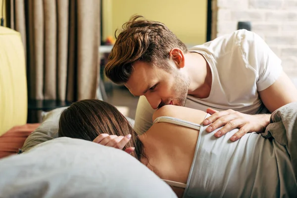 Selective focus of handsome man kissing shoulder of girlfriend in bed — Stock Photo