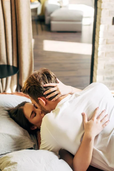 Mujer con los ojos cerrados besando novio barbudo en la cama - foto de stock