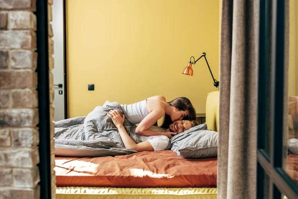 Selective focus attractive woman kissing cheerful boyfriend in bed — Stock Photo