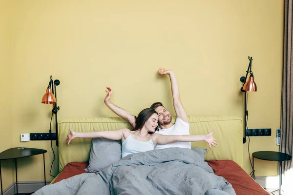 Cheerful man and woman stretching in bed — Stock Photo