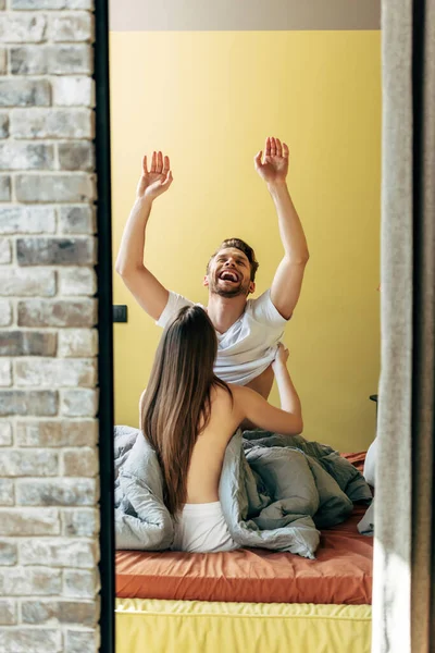 Vista trasera de la joven mujer desnudándose hombre sonriente en el dormitorio - foto de stock