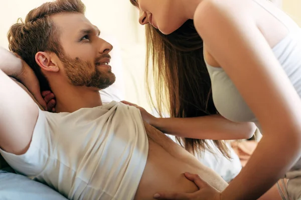 Весела жінка торкається м'язистого чоловіка в спальні — стокове фото