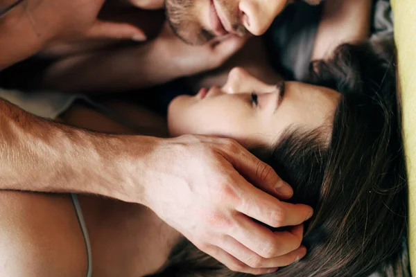 Вид сверху босого мужчины, трогающего лицо девушки с закрытыми глазами в спальне — стоковое фото