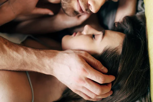 Vista dall'alto dell'uomo barbuto che tocca il viso della ragazza con gli occhi chiusi in camera da letto — Foto stock