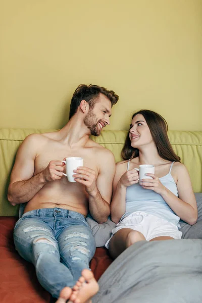 Enfoque selectivo de pareja feliz mirándose y sosteniendo tazas con café - foto de stock