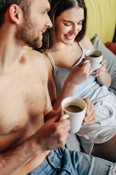 Избирательный фокус веселой пары, держащей чашки с кофе — стоковое фото
