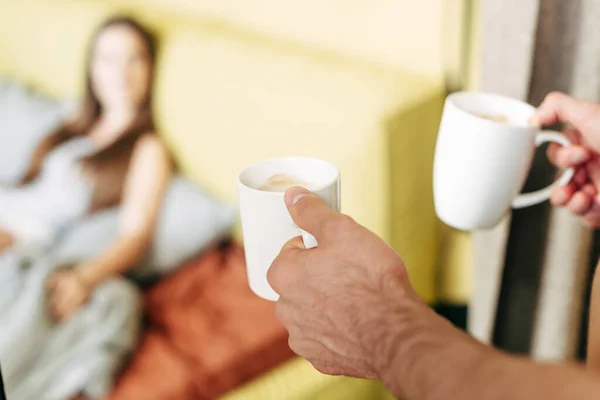 Enfoque selectivo del hombre sosteniendo tazas blancas cerca de la mujer en la cama - foto de stock