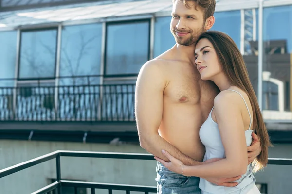 Homme heureux et torse nu étreignant avec une femme attrayante sur le balcon — Photo de stock