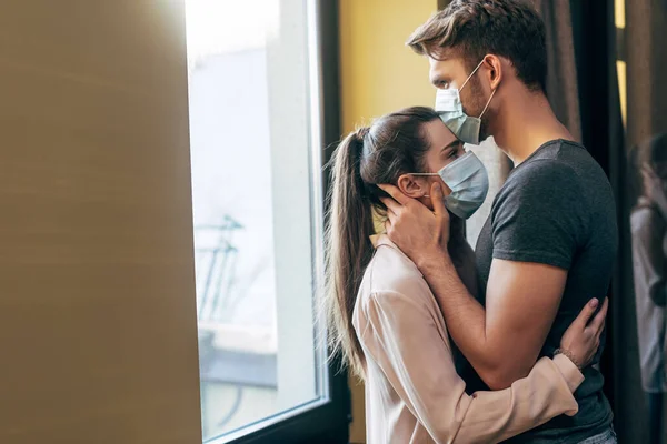 Foco seletivo do homem na máscara médica beijando a testa da mulher em casa — Fotografia de Stock