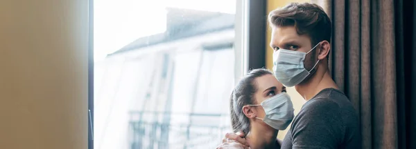 Orientación panorámica de la mujer en máscara médica mirando novio en casa - foto de stock